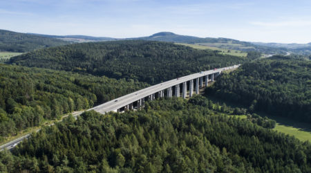 A panoramic aerial view of a highway bridge among vast amounts of greenery.